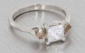 Platinum princess cut three stone ring set with champagne diamonds on the shoulders
