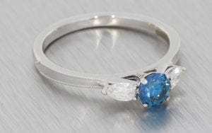 Three stone ring featuring a treated blue diamond,  framed With stunning pear shaped diamonds