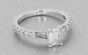 Art Deco style platinum ring with a step cut diamond trilogy and diamond set shoulders