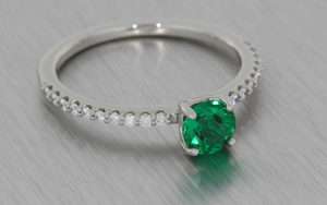 Dainty platinum ring set with a round emerald and diamond shoulders
