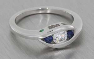 Bypass style white gold trilogy ring set with a a round brilliant diamond with two round sapphires either side